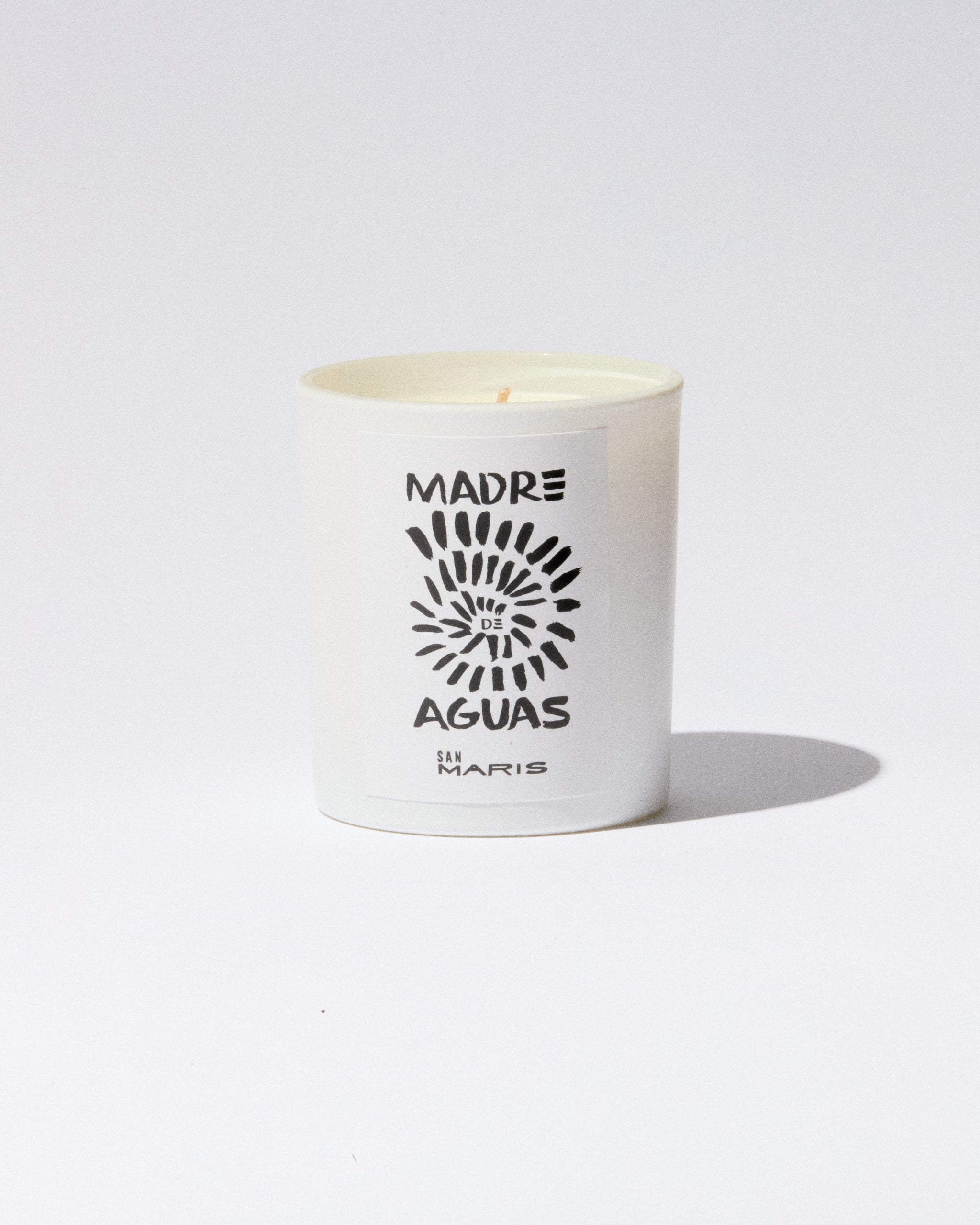 White candle with 'Madre de Aguas' branding on a light gray background