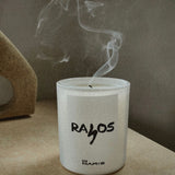 Candle with 'RAYOS' branding on a surface with smoke rising