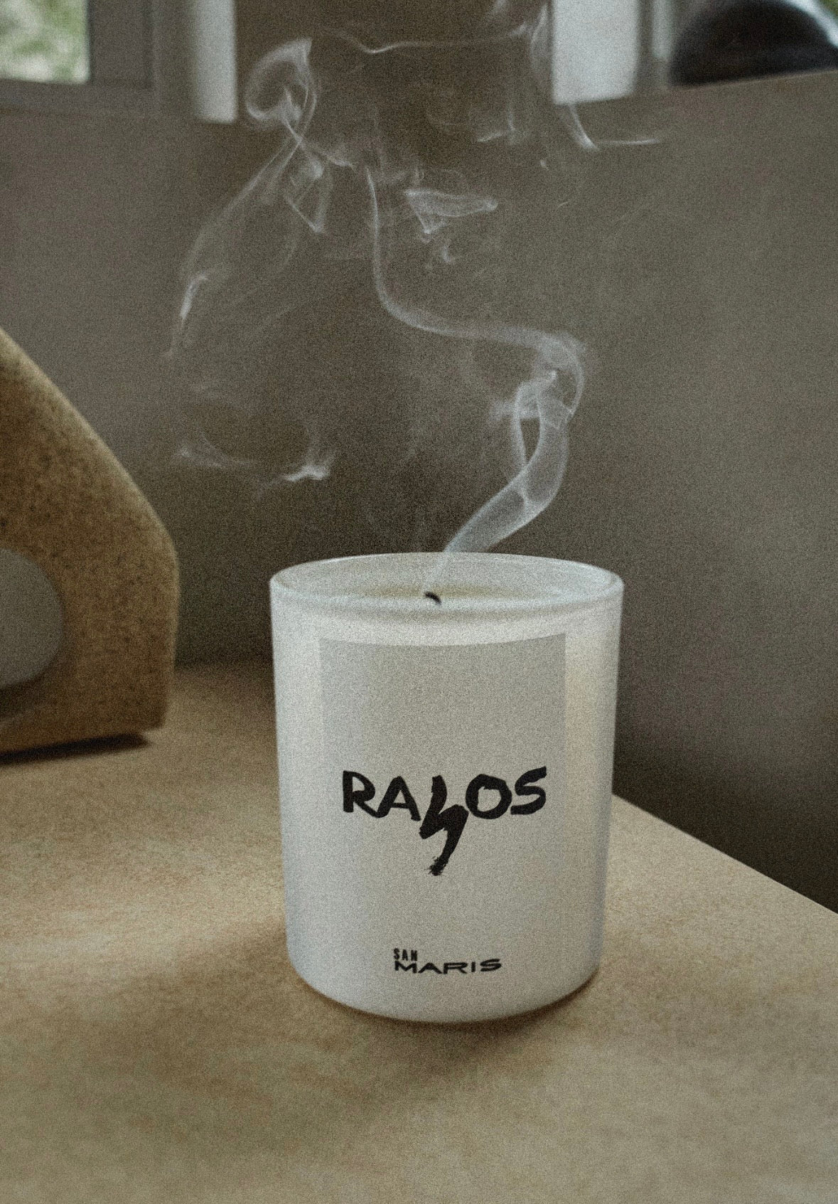 Candle with 'RAYOS' branding on a surface with smoke rising
