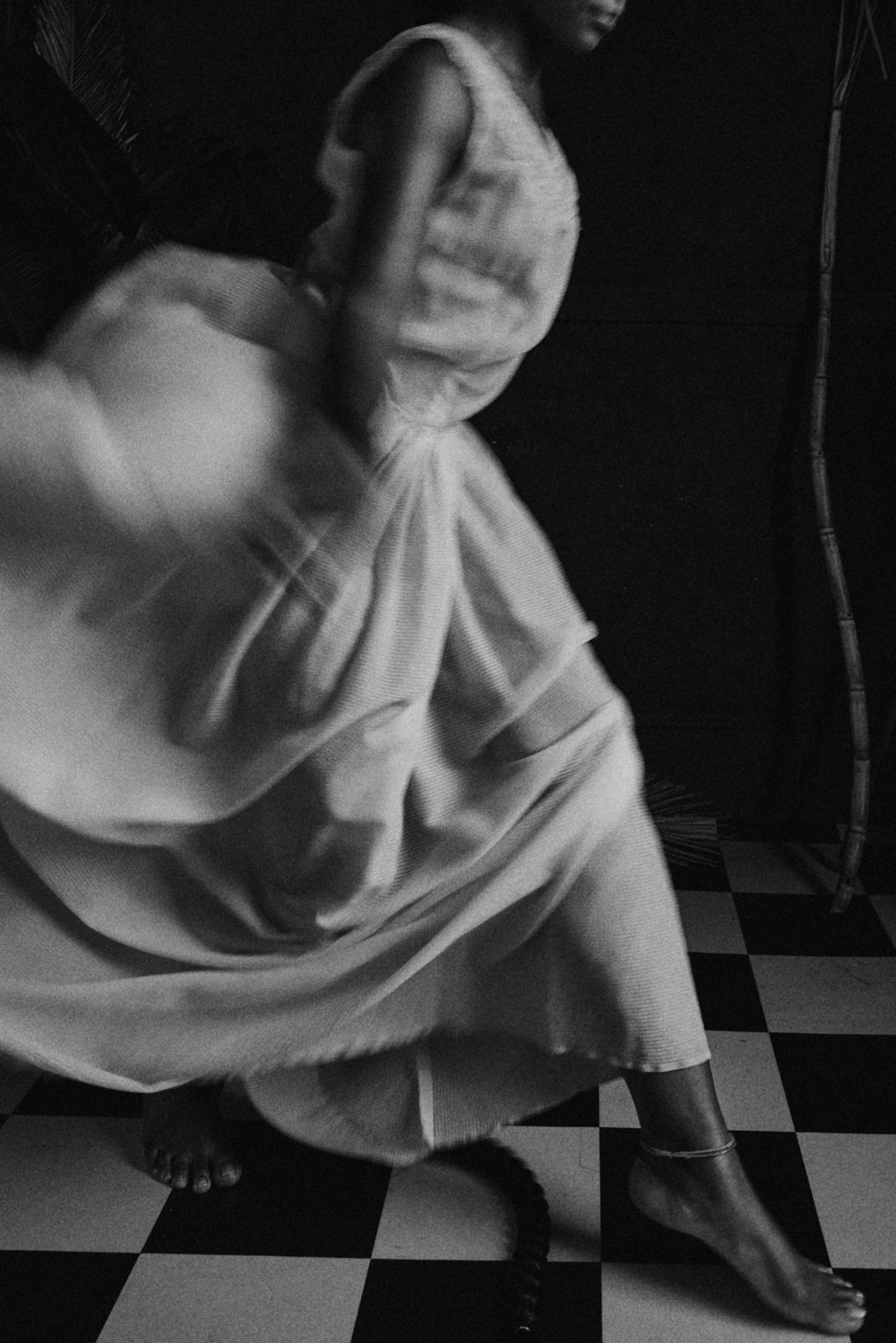 Person dancing on a checkered floor with a draped garment