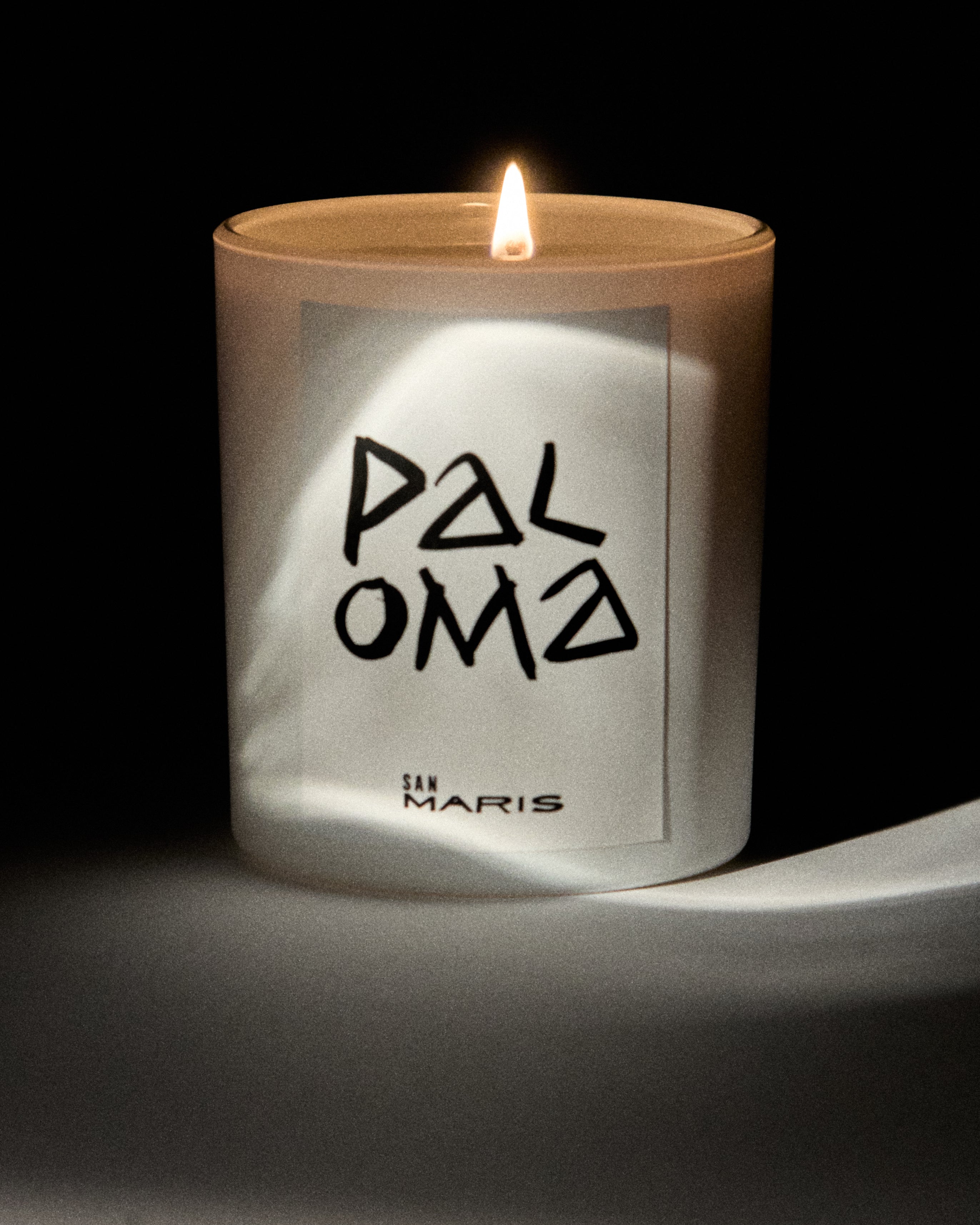 Candle with 'Paloma' and 'San Maris' branding on a dark background