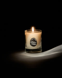 Caminos mini candle by San Maris lit and glowing on a draped white cloth against a black background