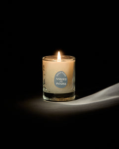 Madre de Aguas mini candle by San Maris lit and glowing on a draped white cloth against a black background
