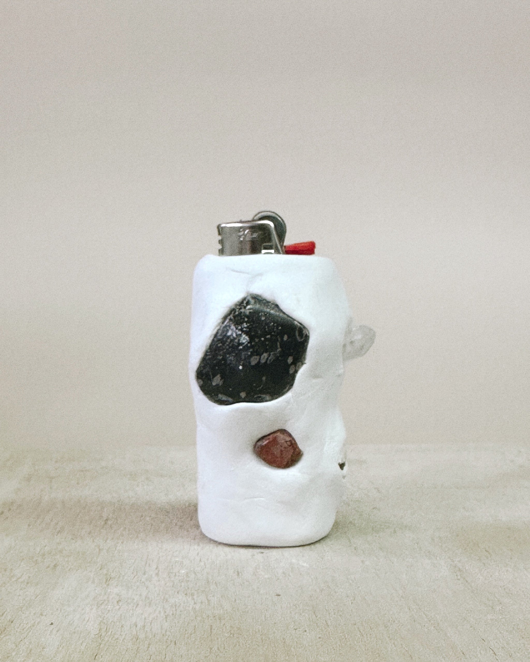 White ceramic lighter with embedded stones on a beige surface