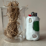 Glass container with vetiver and a white ceramic lighter with green accents on a neutral background