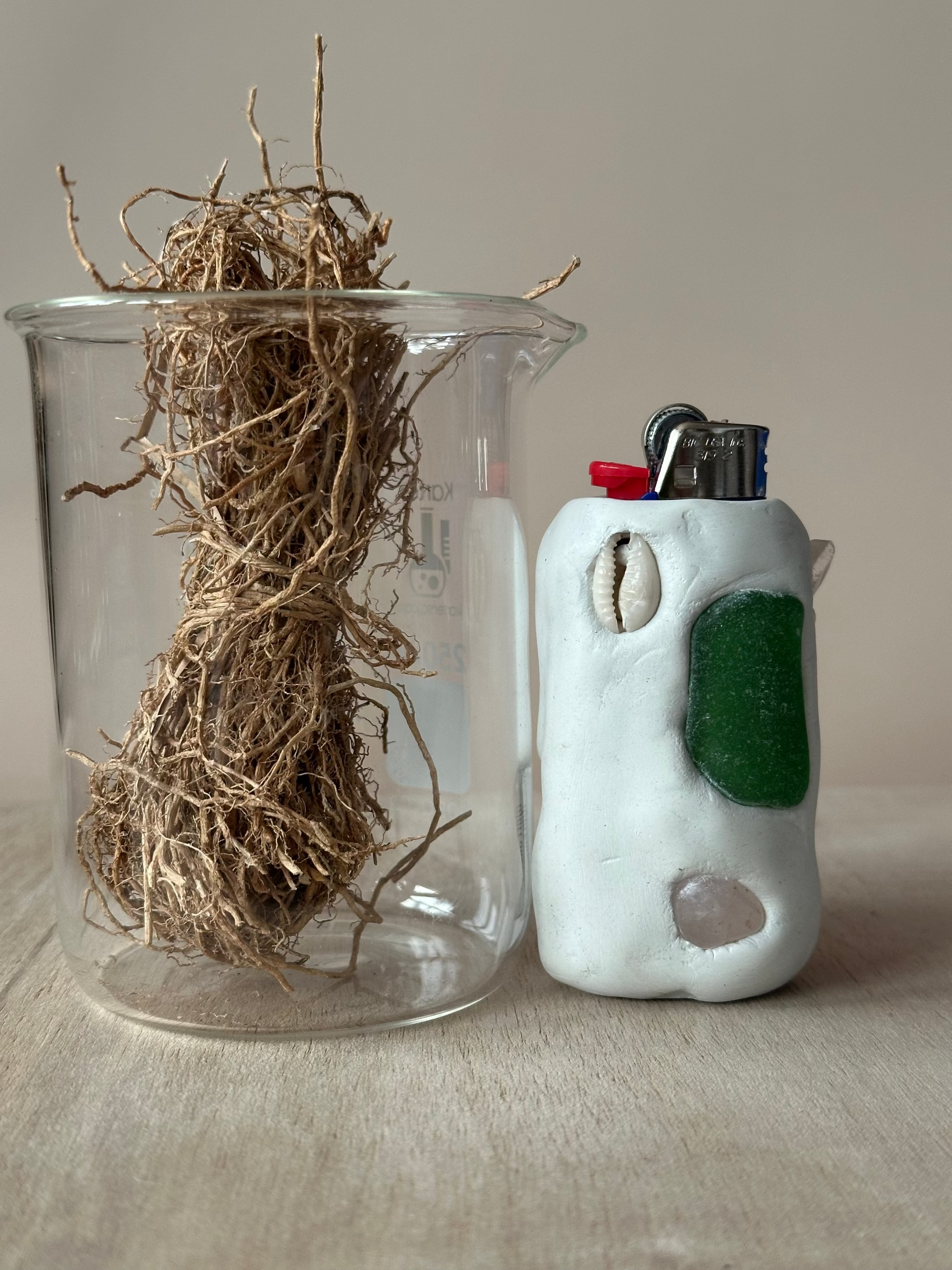 Glass container with vetiver and a white ceramic lighter with green accents on a neutral background