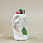 White ceramic shaped object  lighter with a green glass lighter on a beige background