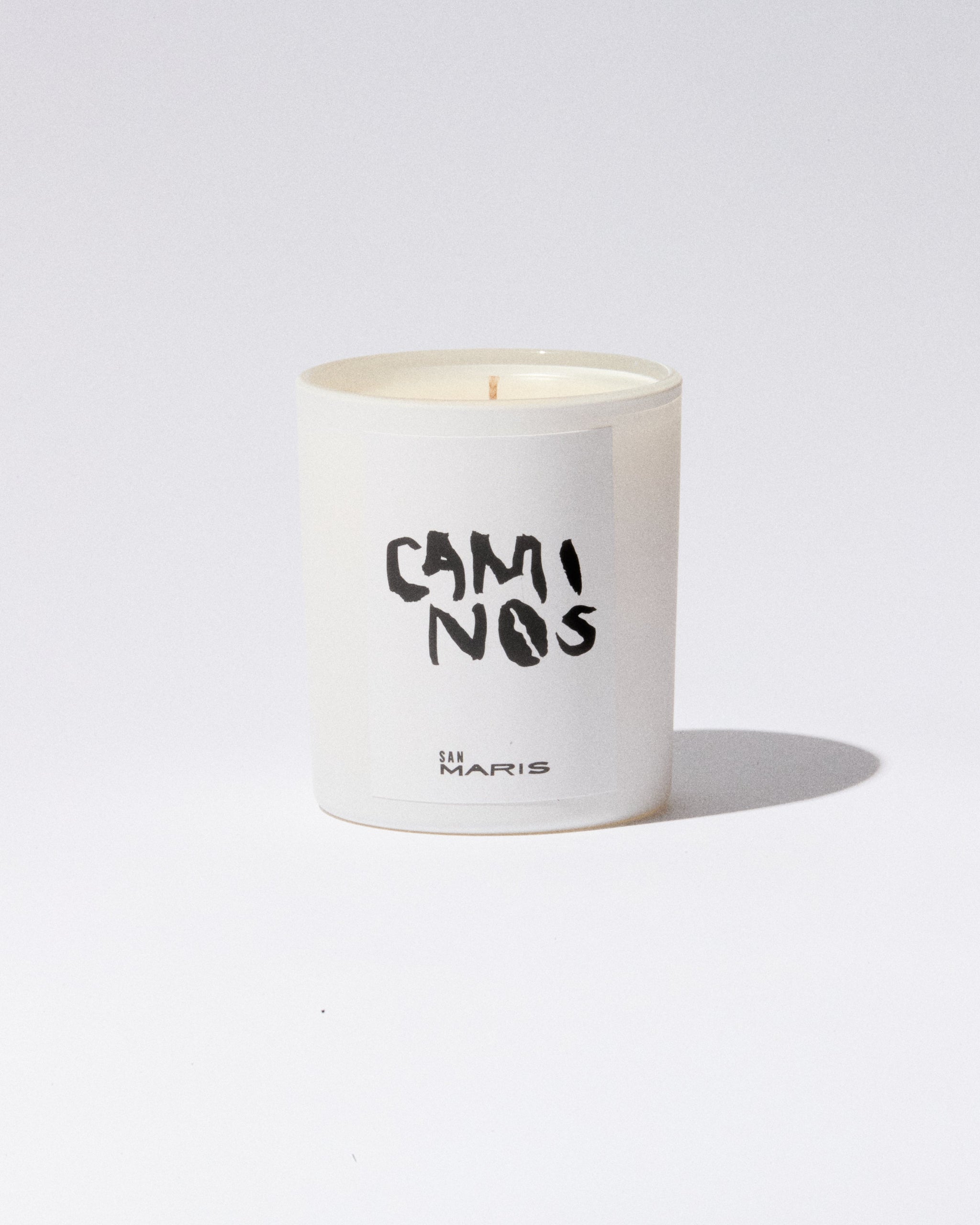 White candle in a container with 'CamiNos' branding on a light gray background