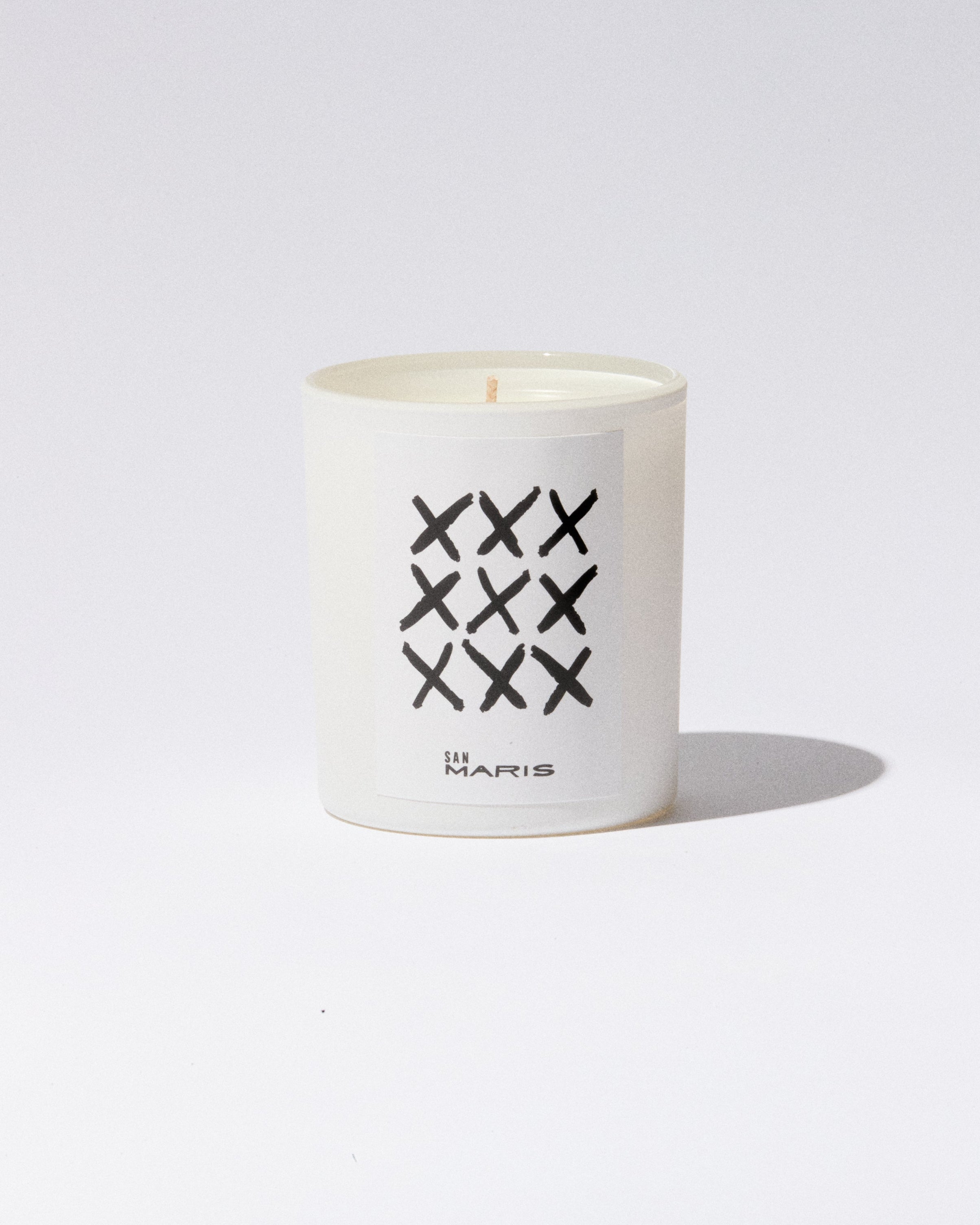 Oyá ritual candle by San Maris in a white glass vessel with hand-drawn X marks
